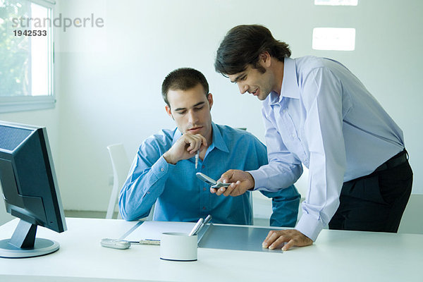 Zwei junge Geschäftsleute im Büro  die mit dem Handy nach unten schauen.