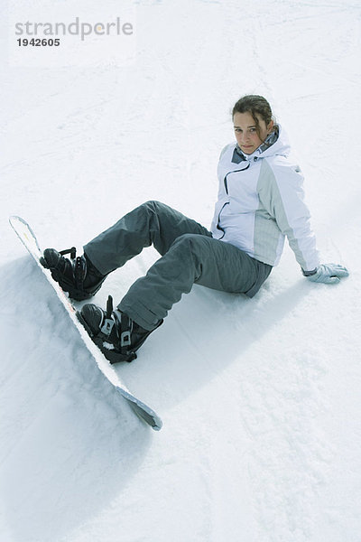Junger Snowboarder sitzt auf dem Boden und schaut in die Kamera.