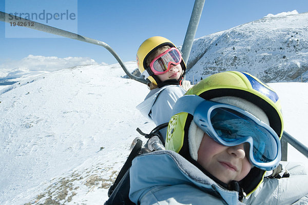 Zwei junge Freunde auf dem Skilift  beide mit Skibrille  einer mit Blick auf die Kamera.
