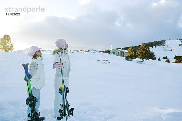 Zwei junge Freunde stehen zusammen  halten Skier und schauen weg.