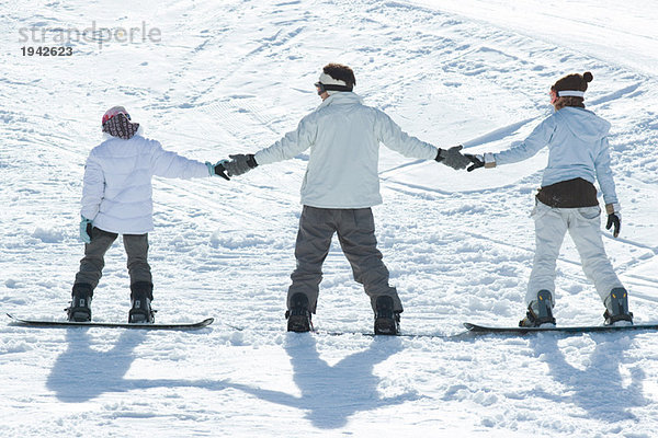 Drei junge Snowboarder stehen zusammen  halten Händchen  Rückansicht