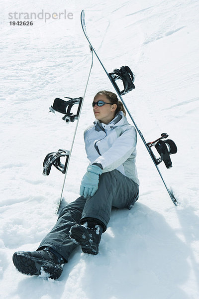 Junge Skifahrerin  die unter den Skiern auf dem Boden sitzt und wegschaut.