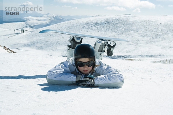 Junger Snowboarder auf dem Boden liegend  Kopf auf den Armen liegend  lächelnd vor der Kamera