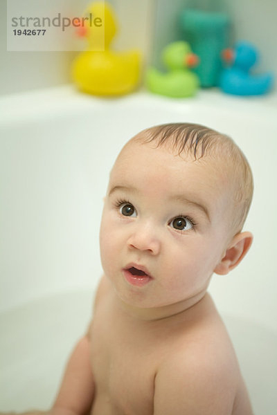 Nacktes Baby in der Badewanne sitzend  aufblickend  große Augen