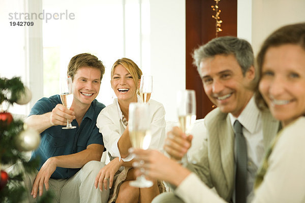 Erwachsene Freunde stoßen mit Champagner an und lächeln in die Kamera.