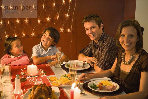 Familie mit zwei Kindern beim festlichen Abendessen  lächelnd vor der Kamera