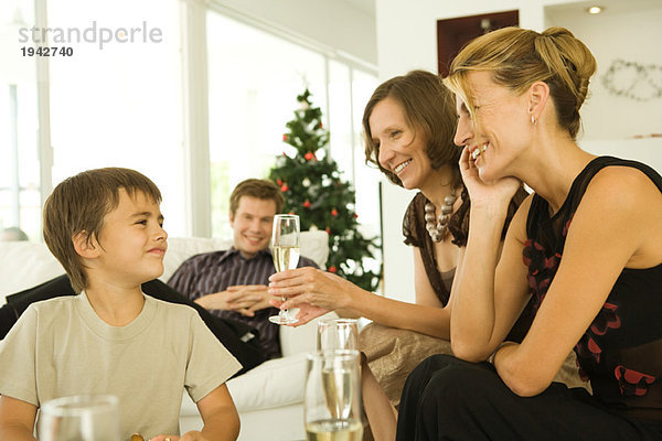 Drei Erwachsene trinken Champagner  lächeln den Jungen an  Weihnachtsbaum im Hintergrund
