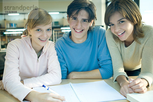 Drei Studenten studieren zusammen und lächeln vor der Kamera.