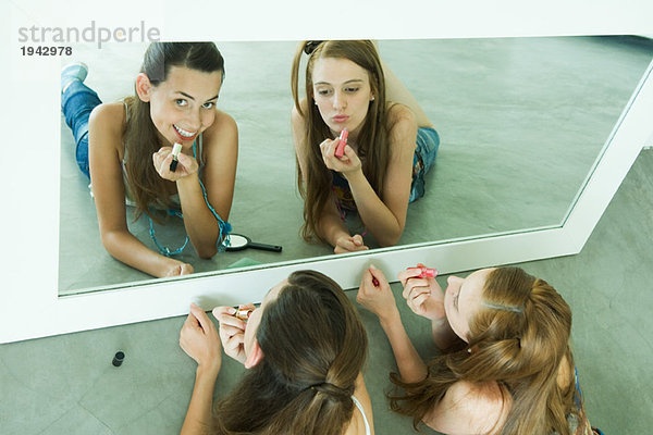 Zwei Freunde auf dem Boden liegend  Lippenstift auftragend  in den Spiegel schauend  einer in die Kamera schauend