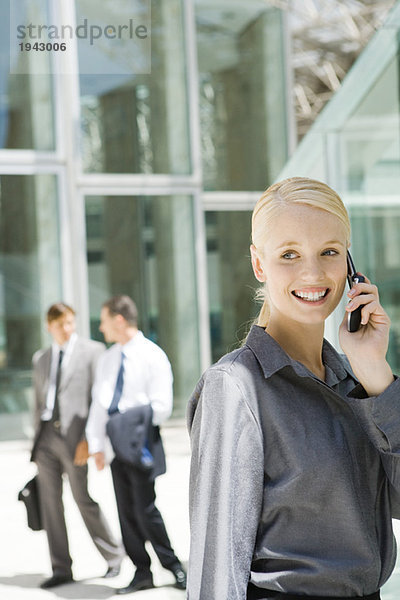 Junge Geschäftsfrau mit dem Handy  schaut weg  Mitarbeiter im Hintergrund