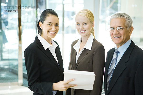 Geschäftspartner lächeln vor der Kamera  eine Frau hält einen Stapel Dokumente in der Hand.