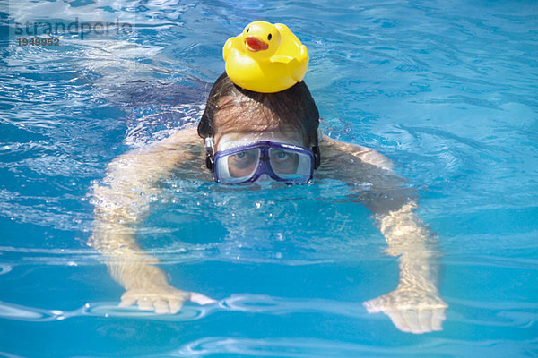 Ein Mann schwimmt mit einer Badeente auf dem Kopf.
