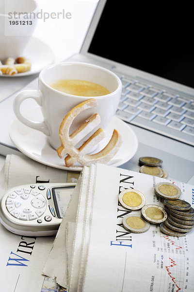 Tasse Kaffee  Euro-Cookie  Münzen  Zeitung und Handy vor dem Laptop