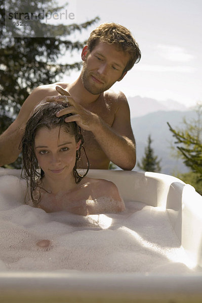 Young woman lying in bathtub  young man washing hair