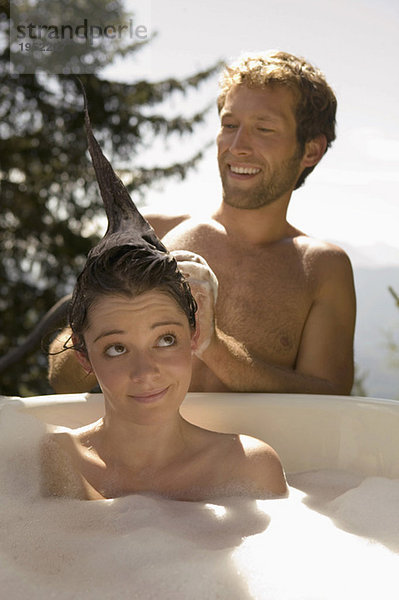 Young woman lying in bathtub  young man washing hair