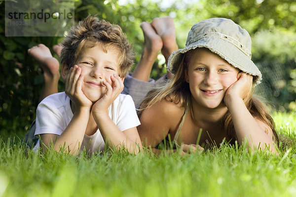 Junge und Mädchen (6-9) auf Gras liegend  Portrait