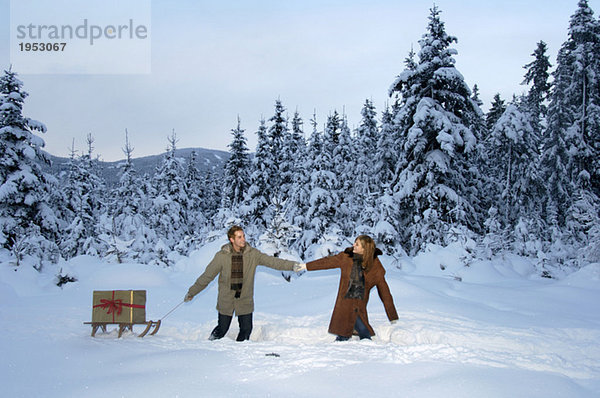 Junges Paar mit Weihnachtsgeschenk auf Schlitten im Schnee