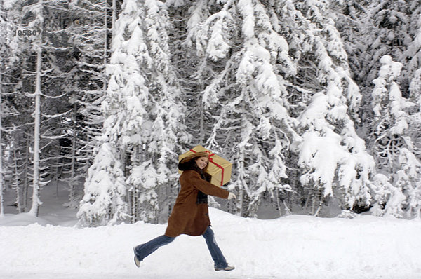 Junge Frau mit Weihnachtsgeschenk auf den Schultern im Schnee  lächelnd