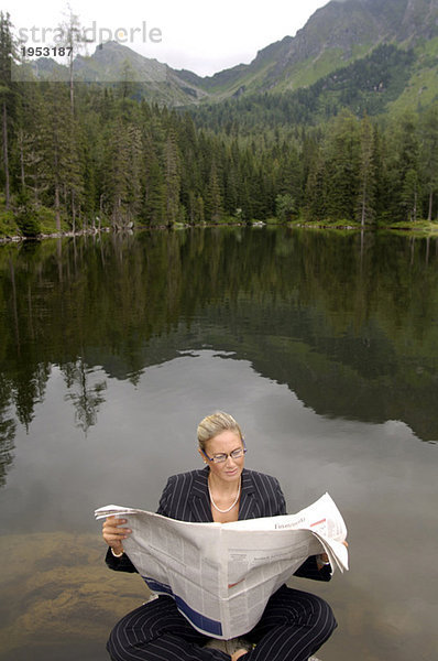 Geschäftsfrau liest Zeitung am See