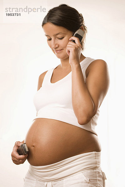 Schwangere Frau hält Tasse an Bauch und Ohr