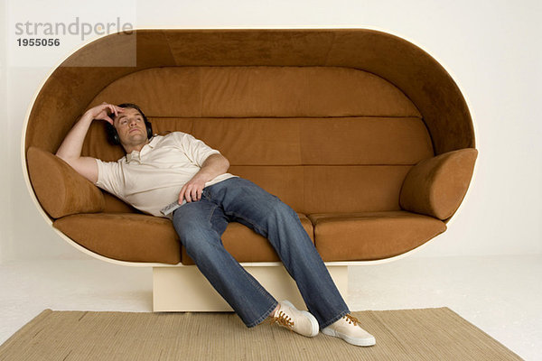 Mann entspannt auf dem Sofa mit Kopfhörer und Fernbedienung
