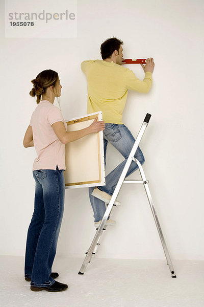 Young couple hanging up painting  man standing on ladder