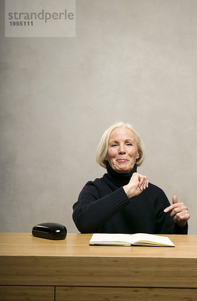 Seniorin am Tisch sitzend mit Buch  lächelnd