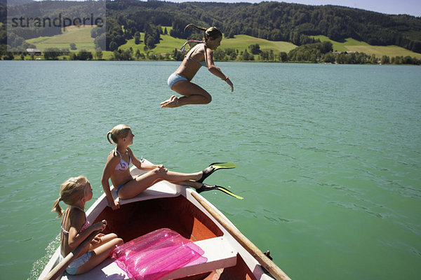 Mädchen (8-15) auf dem Boot sitzend  eine springt im Wasser  Seitenansicht