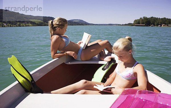 Mädchen (13-15) sitzen auf dem Boot  lesen  Seitenansicht