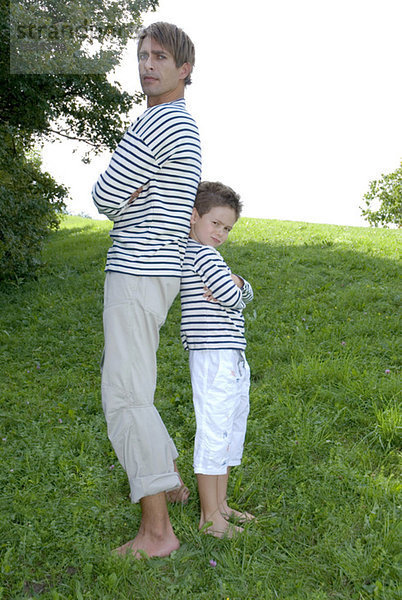 Vater und Sohn (4-7) im Park stehend  Rücken an Rücken