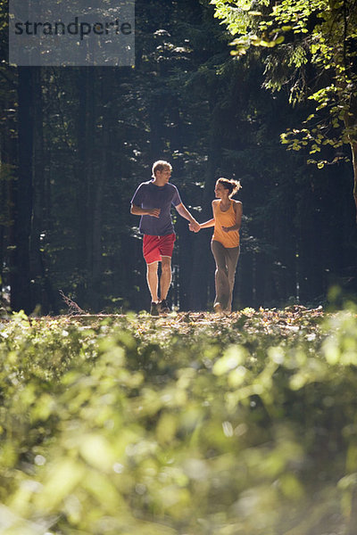 Junges Paar beim Joggen im Wald  Händchen haltend