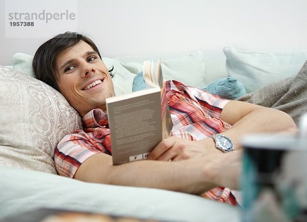 Kerl liegt in der Couch und liest das Buch.