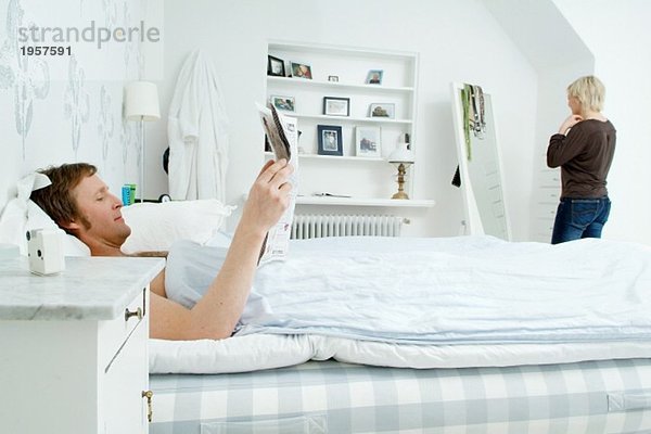 Mann bleibt im Bett und liest Zeitung