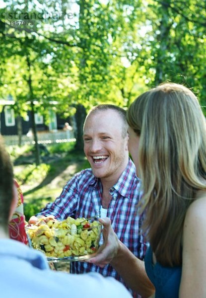 Ein Typ  der eine Schüssel Salat über den Tisch führt.