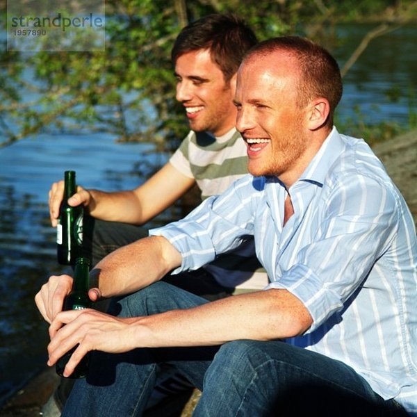 Zwei Kerle sitzen auf einem Felsen und trinken Bier.