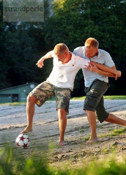 Zwei Kerle kämpfen um einen Fußball am Strand.