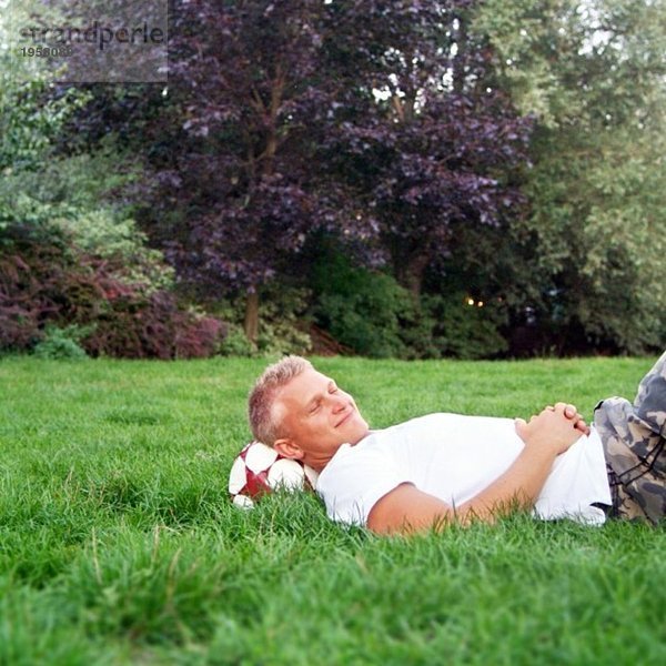 Ein Kerl  der in einem Park liegt und sich nach dem Fußballspielen ausruht.