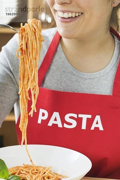 Junge Frau mit Schürze isst Spaghetti mit Tomatensauce