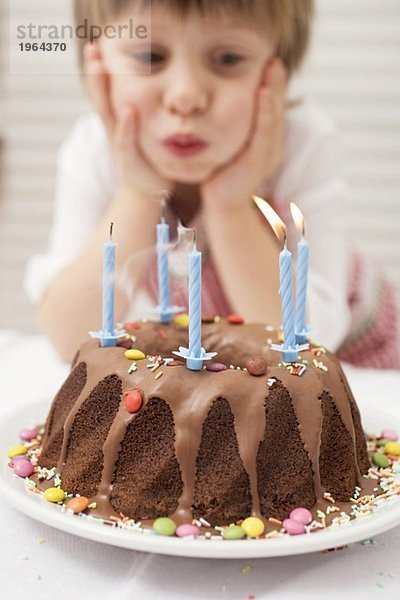 Kleiner Junge bläst Kerzen am Geburtstagskuchen aus