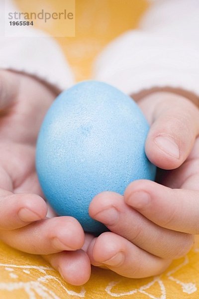 Kinderhände halten blau gefärbtes Ei