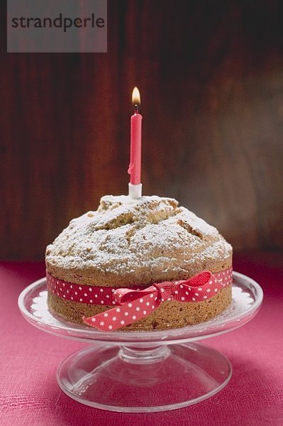 Geburtstagskuchen mit roter Schleife und brennender Kerze