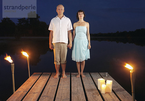 Paar  stehen abends nebeneinander auf Steg an See