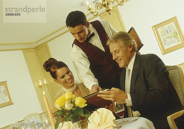 Paar  elegant  im Restaurant  Kellner zeigt in Weinkarte