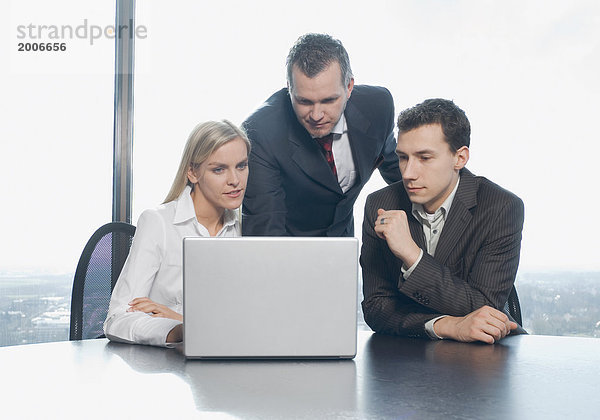 Zwei Männer und eine Frau im Büro an Laptop