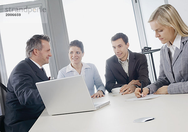 Zwei Männer und zwei Frauen sitzen im Büro an Schreibtisch  Besprechung