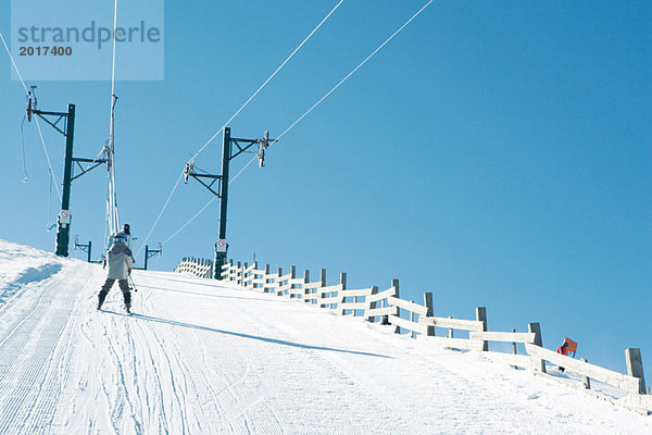 Junger Skifahrer beim Aufstieg mit dem Skilift  Rückansicht