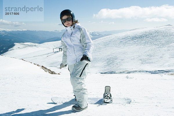 Teenagermädchen stehend mit Snowboard  lächelnd vor der Kamera  Ganzkörperporträt