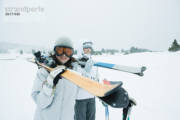 Zwei junge Skifahrer gehen zusammen  tragen Skier auf den Schultern  einer schaut in die Kamera....