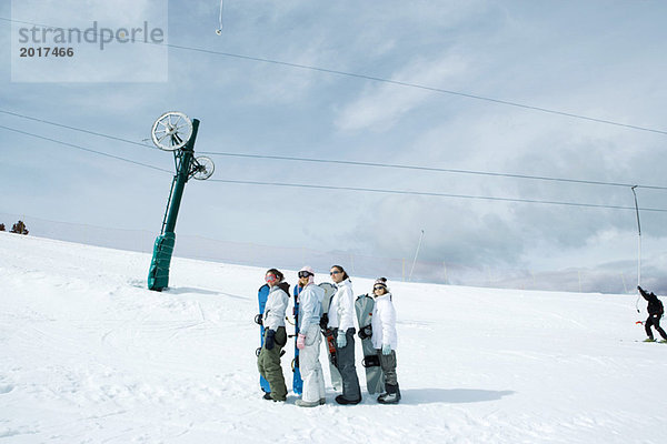 Vier junge Snowboarder stehend  aufgereiht  aufschauend  Mitteldistanz