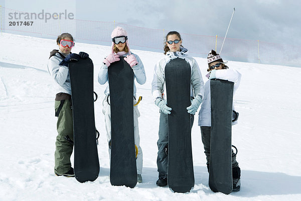 Vier junge Freunde stehen zusammen  halten Snowboards und schauen in die Kamera.